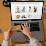 hands holding a debit card while at a laptop. The screen shows a women's clothing shopping site