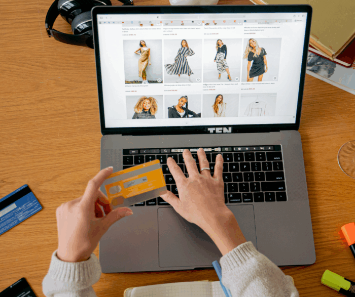 hands holding a debit card while at a laptop. The screen shows a women's clothing shopping site